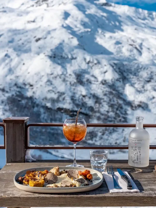 ssiette et cocktail sur la terrasse de Chez Pépé Nicolas, face aux montagnes enneigées de la vallée des Belleville.